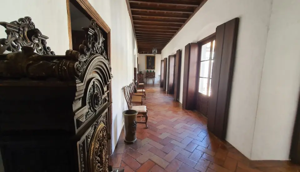Palacio de los Rueda (Carmona) 1 Pasillo antiguo con sillas y ventanas grandes.