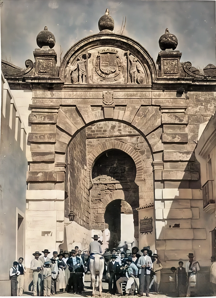 puerta sevilla a color Arco histórico con personas y caballo en pueblo español.